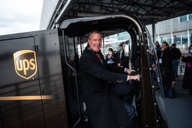 Mayor Bill de Blasio grins as he sits inside a brown micro-truck with the UPS logo